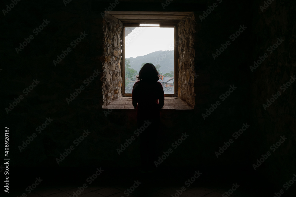 Silhouette of lonely woman watching through window