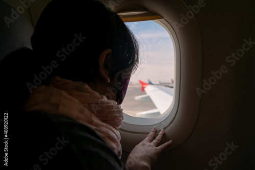 young woman with face mask looking out the window of an airplane