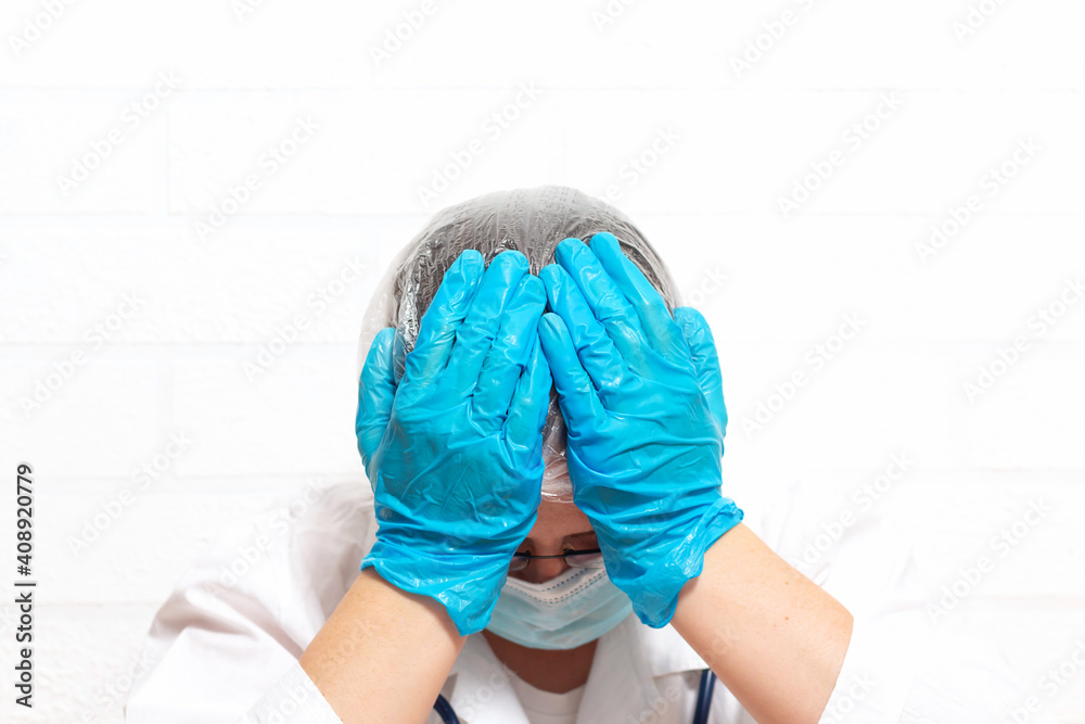 Fototapeta premium Close up of tired exhausted desperate caucasian female doctor in protective uniform. After long shift at hospital doctor covers his face with hands in blue medical gloves.