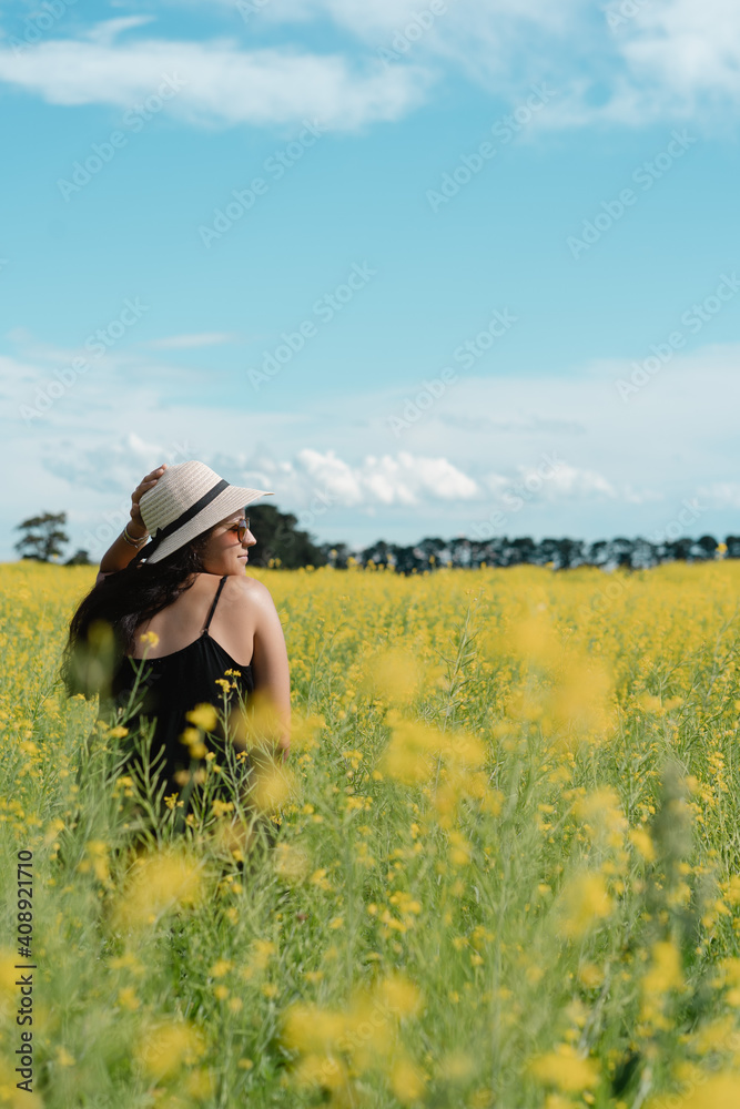 Young woman wearing summer hat posing in profile in yellow field full of flowers
