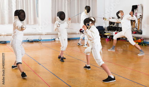 Mixed age group of athletes at fencing coach, training attack movements in duel.