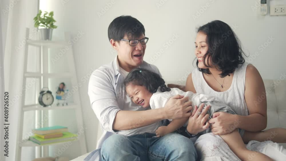 Happy Asian family relaxing at home. Smiling parents embracing and playing with little daughter on sofa in living room. Father and mother with cute child girl kid having fun weekend activity together. Happy Asian family relaxing at home. Smiling parents embracing and playing with little daughter on sofa in living room. Father and mother with cute child girl kid having fun weekend activity together.