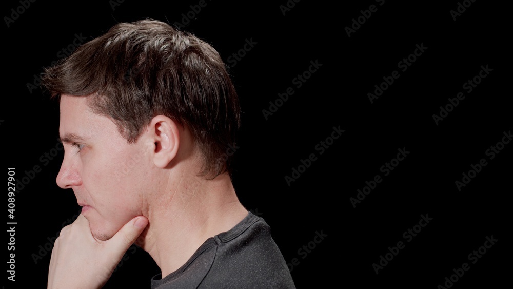 Serious young man thinking. Puzzled with problems. Black background. Side view.