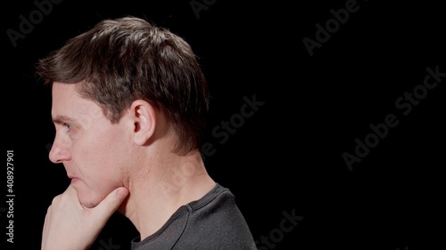 Serious young man thinking. Puzzled with problems. Black background. Side view.