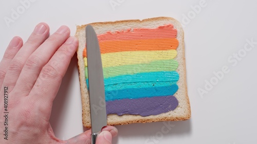 Rainbow. Male spreading colourful paste on a toast with knife. Top view.
