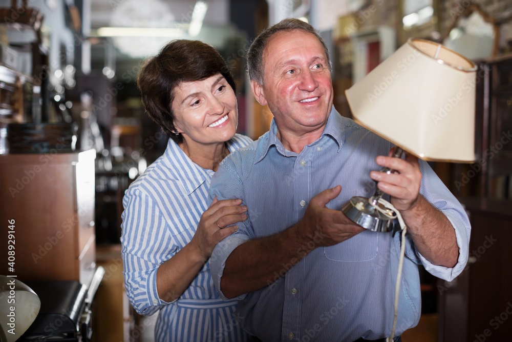 Mature family couple choosing vintage lamp in furniture shop