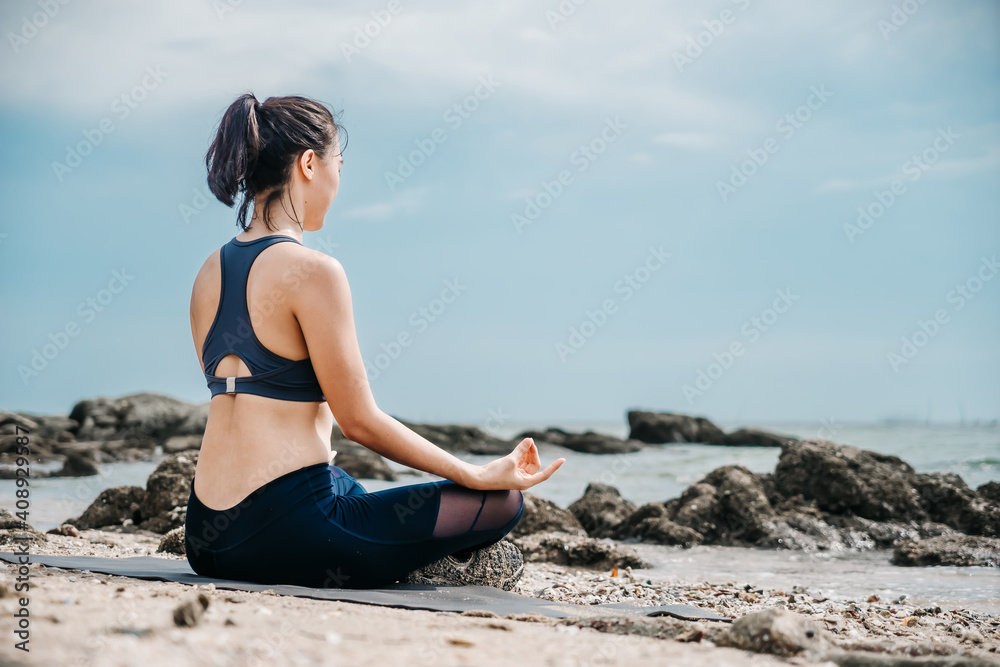 Young Asian woman practicing yoga exercise at quiet rock pier with sea background. Sport and recreation in city rush.