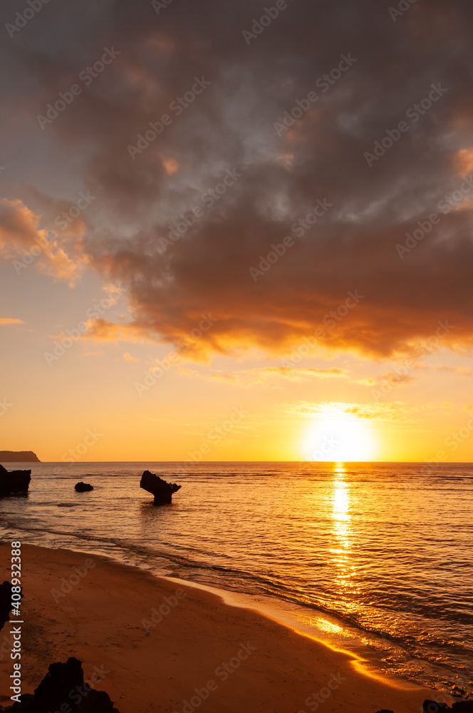 Vibrant sunset reflecting on the sea, colorful clouds over the sun, coastal rocks in the sea. Iriomote Island.
