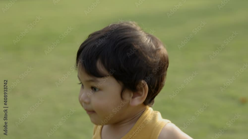 Child walking on the grass. Asian Little boy wear a yellow shirt walking around. Children playing in the playground with sunlight. Child walking on the grass. Asian Little boy wear a yellow shirt walking around. Children playing in the playground with sunlight.