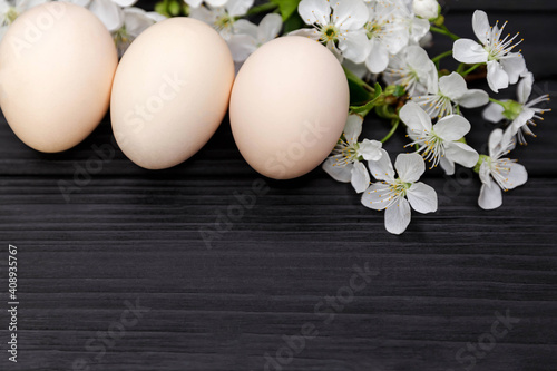 Stylish uncolored easter eggs with cherry flowers branch on dark wooden background in soft light. Eggs natural with branches in blossom. Easter holiday. Copy space for text, top view, flat lay