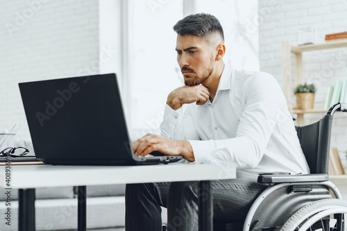 Quadro em tela Serious concentrated man in wheelchair using his laptop for work / seeking a job