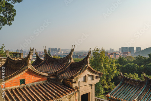 Ancient Chinese temple building with tiled roofs and modern city skyline in the distance
