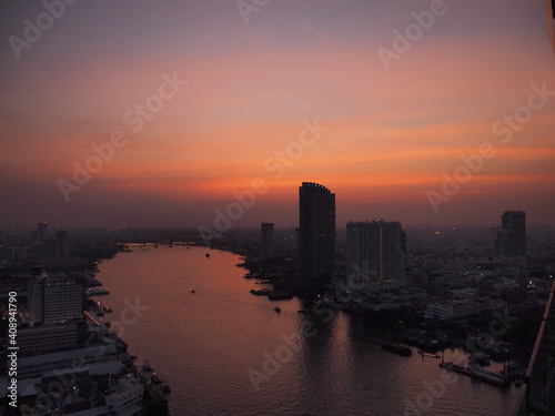 Curve of Chao Phraya River and river side view. In a main business zone of Bangkok. It's combining a contrast of shining buildings and blackening living houses. With a colorful twilight sky.
