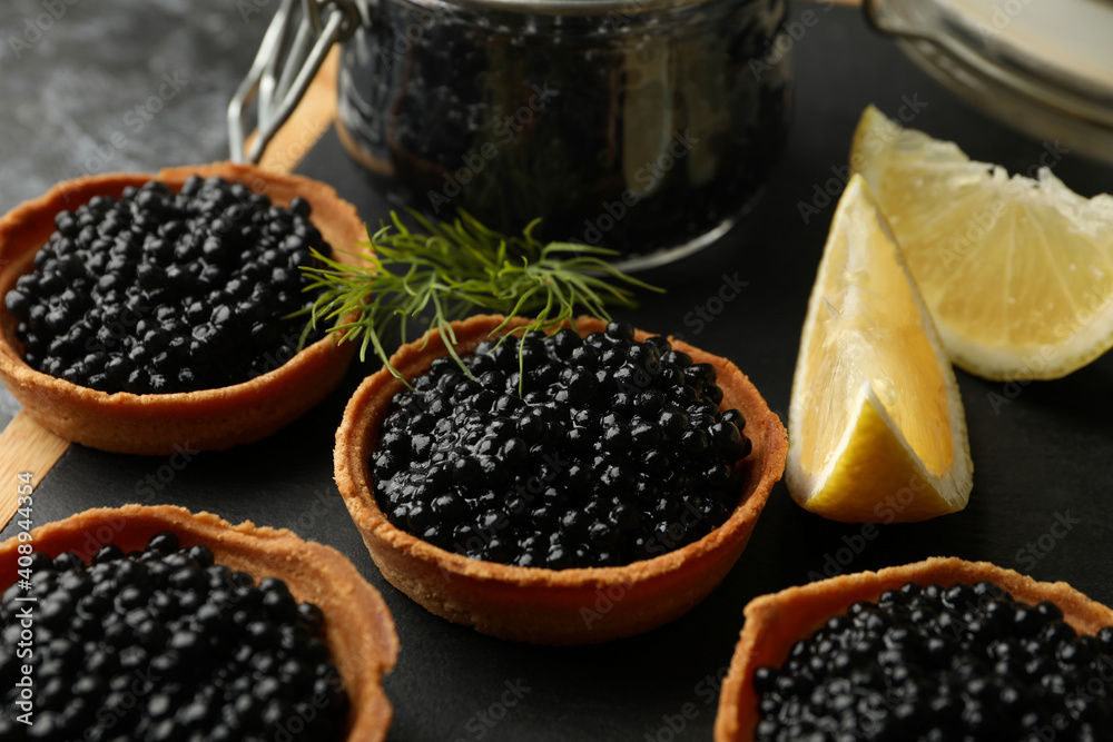 Board with tartlets and jar with caviar on black smokey background, close up Board with tartlets and jar with caviar on black smokey background, close up