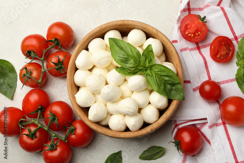 Bowl with mozzarella and basil, tomato and towel on white textured background, top view