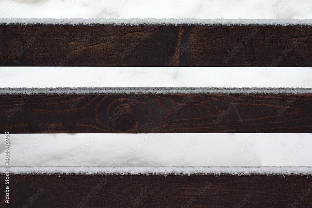 fresh snow on the crossbeams of a wooden bench