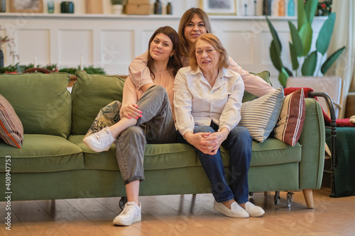 three generations of a family of women are sitting together on the couch. grandmother, daughter, and granddaughter pose together to get a joint photo.