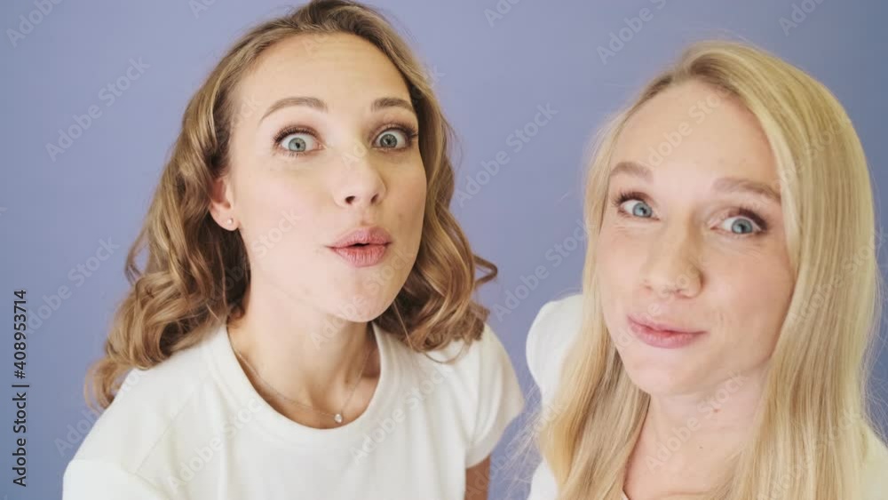 Close-up view of two surprised women are looking to the camera standing isolated over white background in studio Close-up view of two surprised women are looking to the camera standing isolated over white background in studio