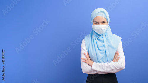 Young muslim woman with hijab wearing a surgical mask over blue background studio.