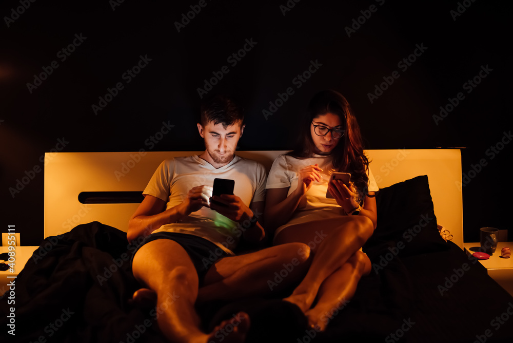 The couple lies in bed and looks into the bodies. Internet addiction problem The couple lies in bed and looks into the bodies. Internet addiction problem