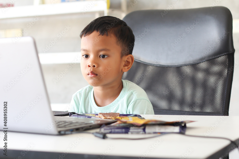 Asian boy kid sitting at table with laptop and preparing to school. Online education concept. Online video call conference class lesson study. Asian boy kid sitting at table with laptop and preparing to school. Online education concept. Online video call conference class lesson study.