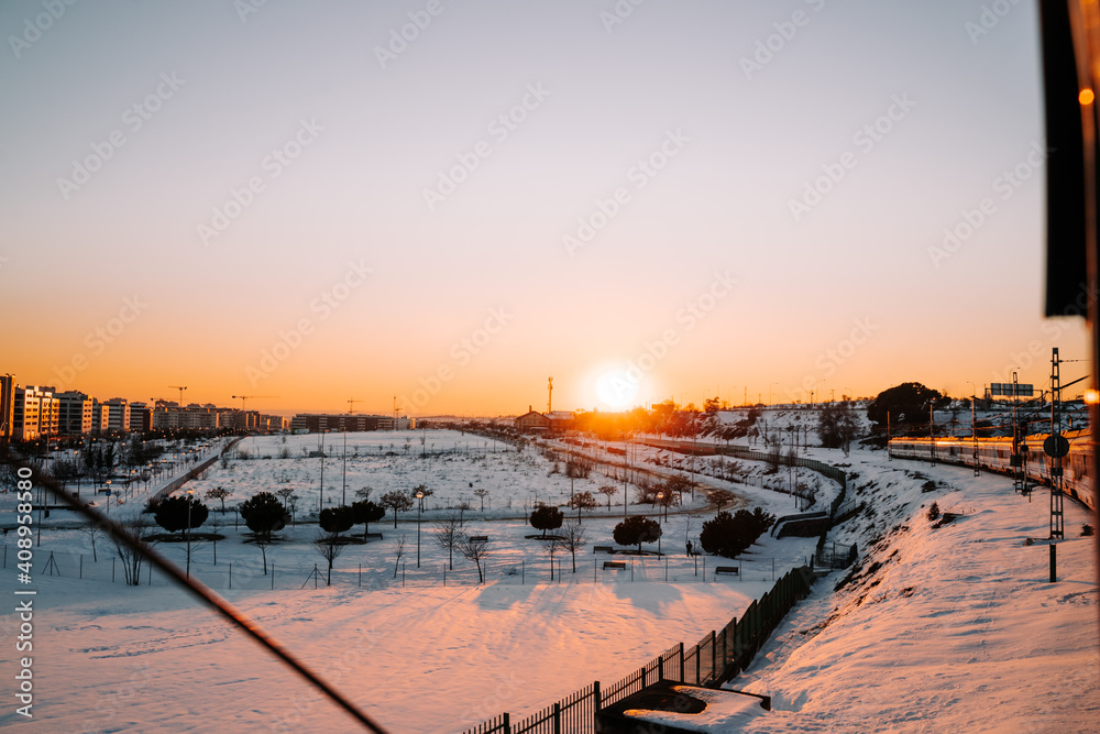 Obraz premium Beautiful view of the city with a lot of snow in the streets from the train while some buildings are illuminated by the sun. Concept of landscape of the snowy city at the sunset.