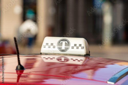 taxi sign on top of a red car roof, defocused street scene in background
