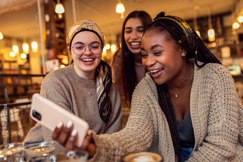 Three young multi ethnic women enjoy coffee at a coffee shop. - obrazy, fototapety, plakaty 