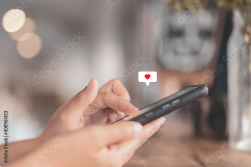 Woman hand using smartphone with heart icon at coffee shop background. Technology business and social lifestyle concept.