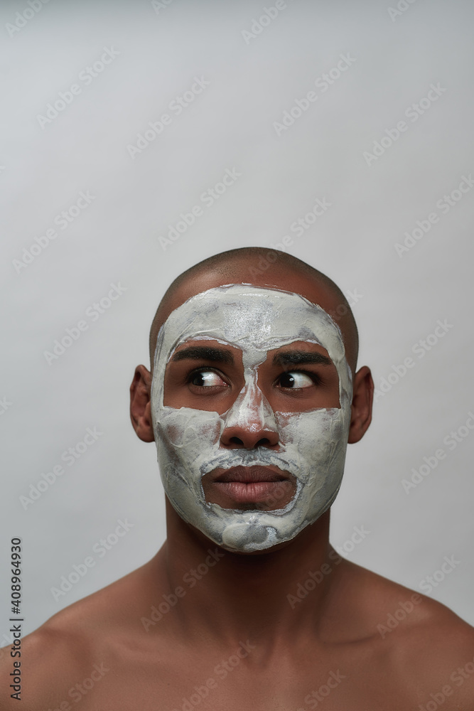 Handsome young african american man looking surprised aside, using facial blackhead removal mask, posing isolated over gray background