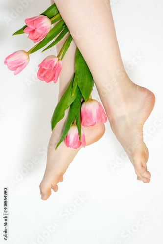 Fototapeta Naklejka Na Ścianę i Meble -  Beautiful slim smooth woman's legs with tulips flowers on white background