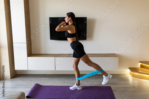 Home workout with resistance band. Woman training at home. Sports woman exercising with resistance band. Strong sporty woman in sportswear. Fitness exercise. Woman watching online tutorials on tablet.