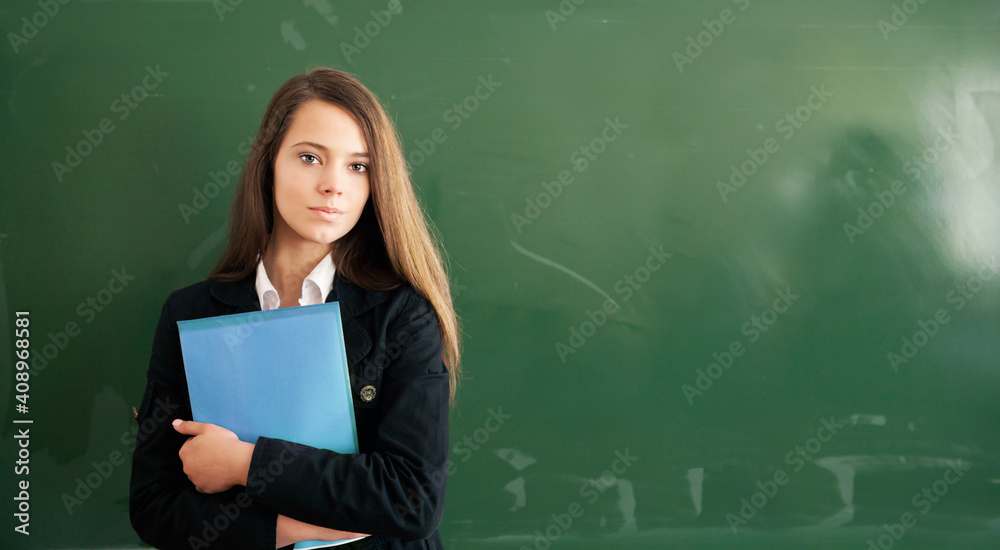 Beautiful girl with folder in hand on school green chalkboard background. Online education and e-learning concept. Back to school, STEM education. Beautiful girl with folder in hand on school green chalkboard background. Online education and e-learning concept. Back to school, STEM education.