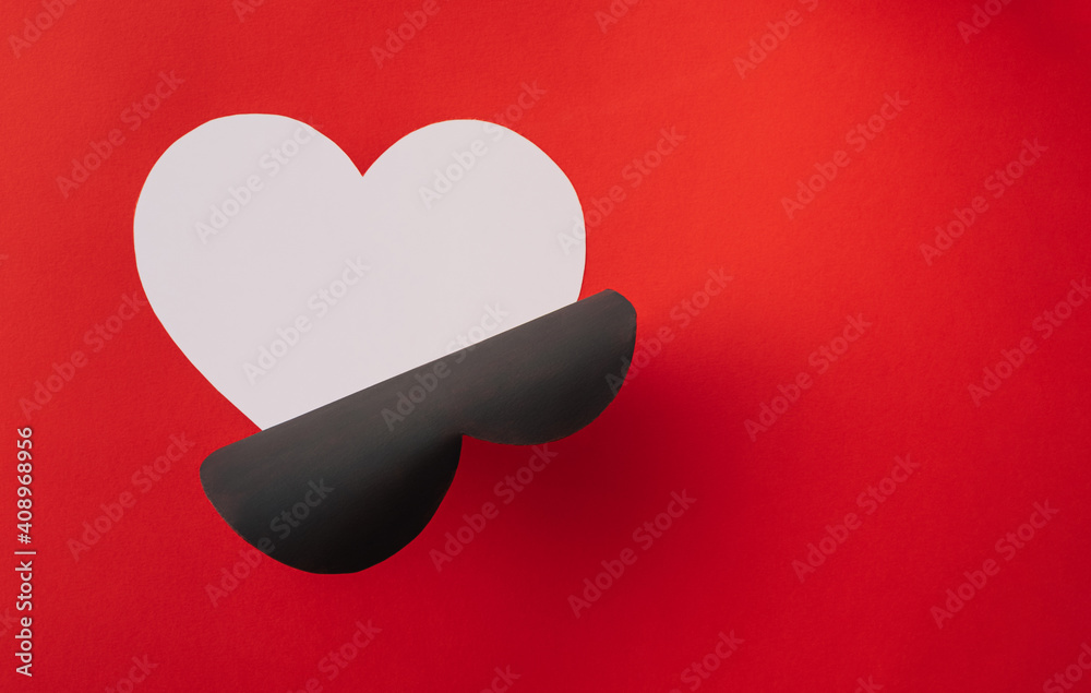 Black heart shape cut to reveal white symbol of love outline on red background Black heart shape cut to reveal white symbol of love outline on red background