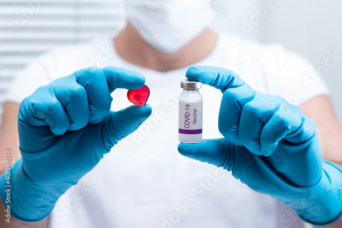 
A medical worker in a mask holds a bottle with the inscription covid-19 vaccine in his hands