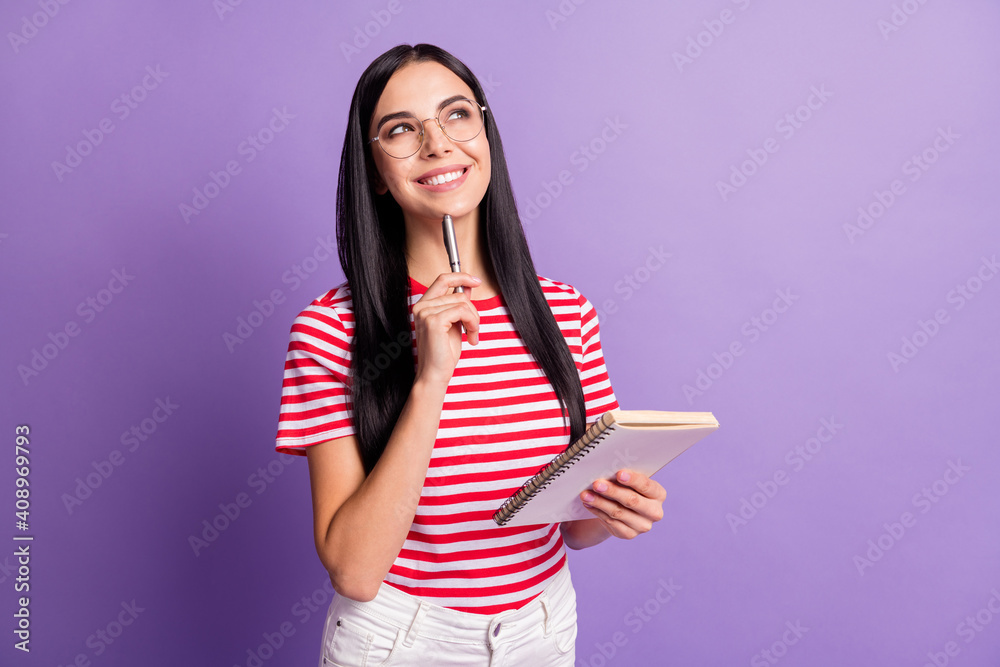 Photo of creative brown haired young woman wear red striped t-shirt hold copybook think article isolated on violet color background Photo of creative brown haired young woman wear red striped t-shirt hold copybook think article isolated on violet color background