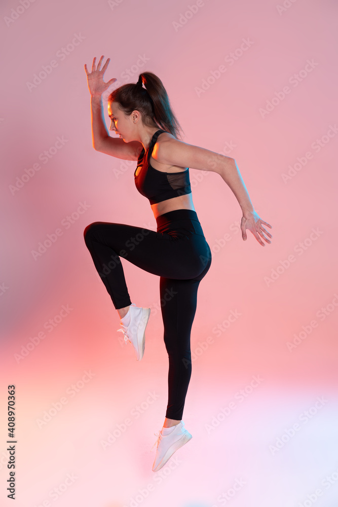 young sporty woman is engaged in crossfit, performs jumps in studio with neon light.
