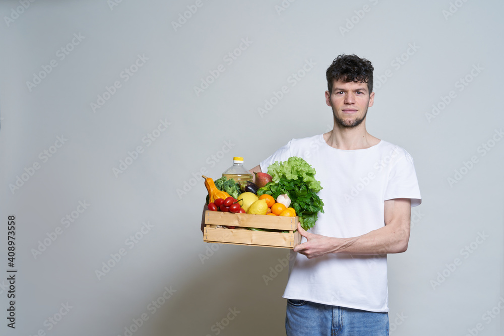online shopping concept. A man in T-shirt holds a box of fresh food in his hands. Food delivery from the supermarket, from farmers. Delivery during quarantine online shopping concept. A man in T-shirt holds a box of fresh food in his hands. Food delivery from the supermarket, from farmers. Delivery during quarantine
