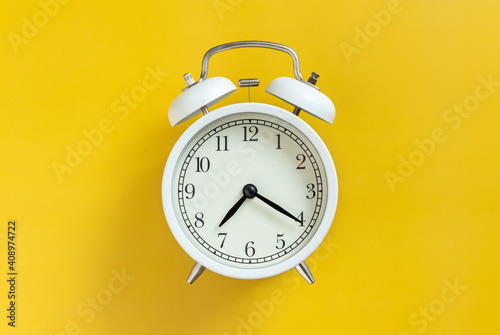 white circle retro classic analog alarm clock with clock needle isolated on yellow empty background with copy space. time management concept.