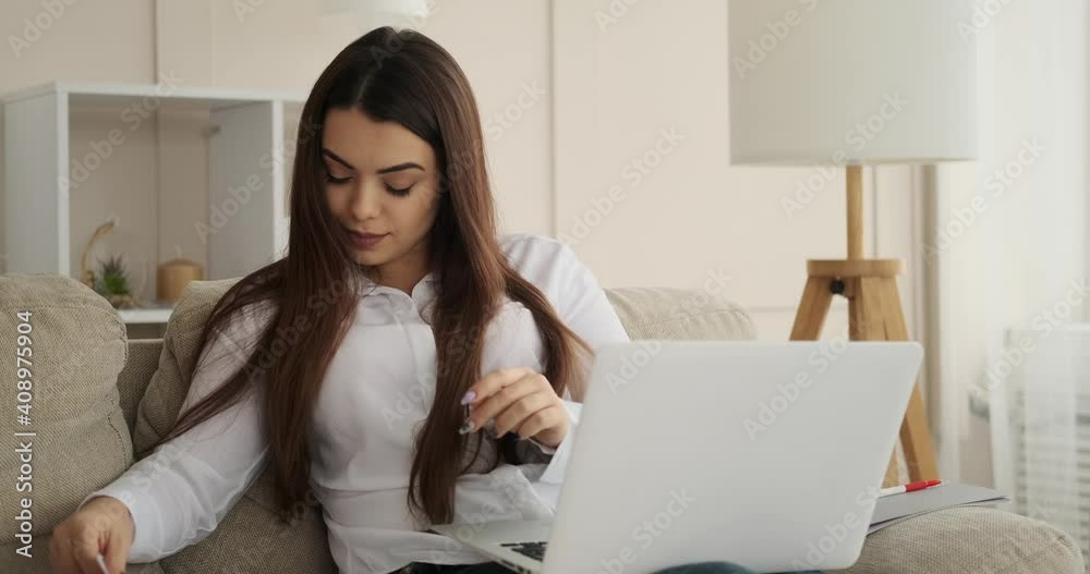 Woman analyzing documents while typing on laptop at home Woman analyzing documents while typing on laptop at home