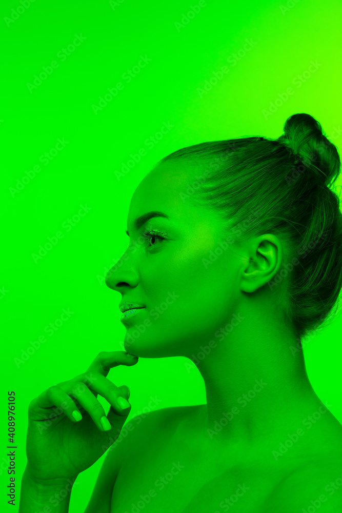 Fototapeta premium Well-kept. Handsome woman's portrait isolated on green studio background in neon light, monochrome. Beautiful female model. Concept of human emotions, facial expression, sales, ad, fashion and beauty.