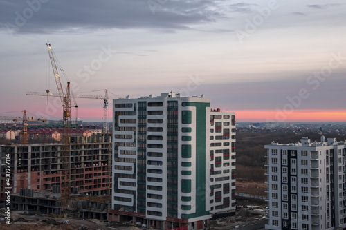 modern multi-apartment high-rise building under construction on the background of construction cranes and the evening sunset sky.