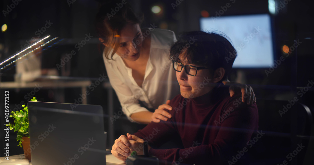 Female executive helping young stressed employee sitting at desk working late in office