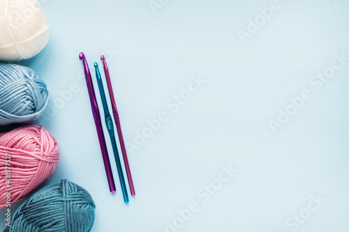 Multicolored crochet hooks with balls of yarn on a blue background with copy space.
