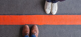 Man and woman standing opposite of each other, divided by a broad red line. Divorce, divide, separation or break-up concept.