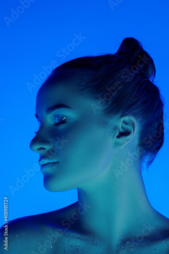Glowing. Handsome woman's portrait isolated on blue studio background in neon light, monochrome. Beautiful female model. Concept of human emotions, facial expression, sales, ad, fashion and beauty.