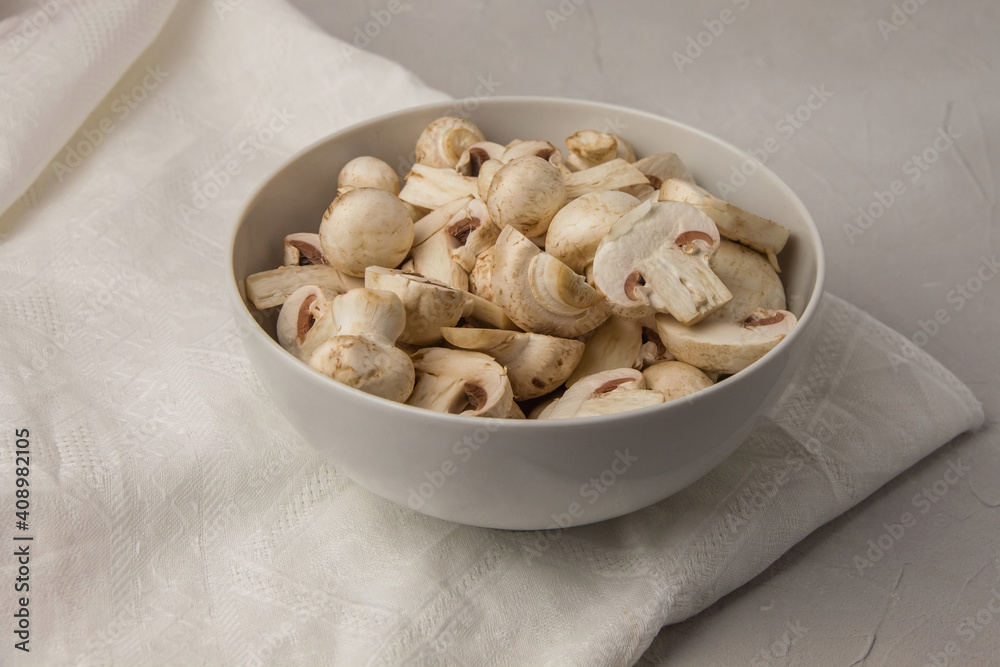 Whole and chopped mushrooms in a round porcelain bowl on a white towel Whole and chopped mushrooms in a round porcelain bowl on a white towel