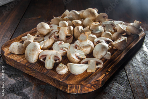 Sliced mushrooms lie on a burnt cutting board on a dark wooden background