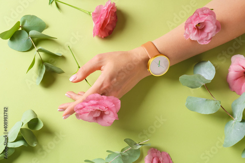 Female hand with stylish wrist watch and flowers on color background
