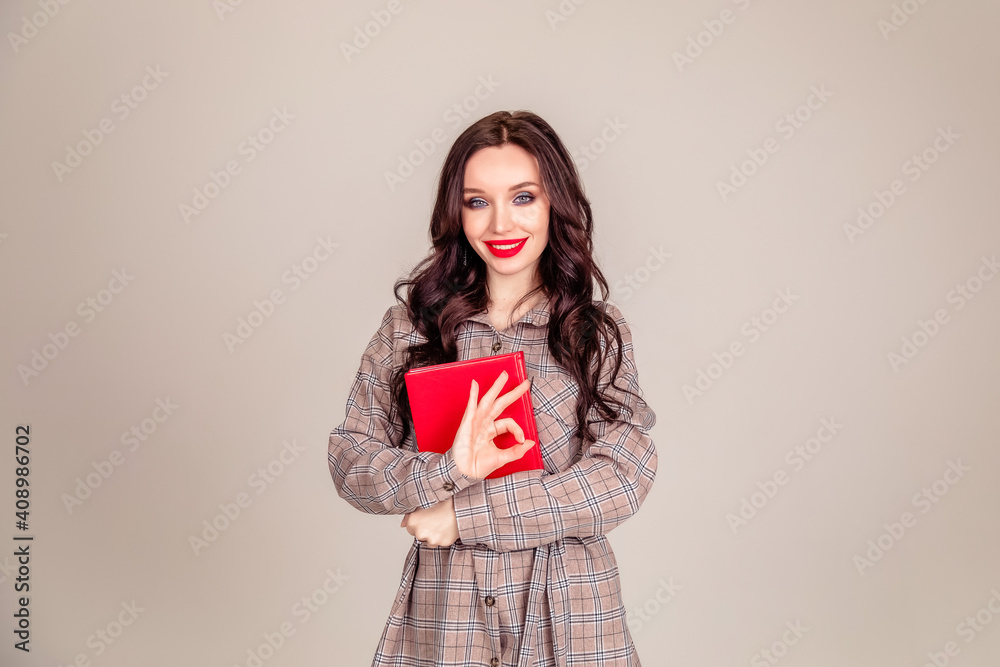 a beautiful young girl with red lips holds a red notebook in her hands. student. businesswoman on isolated gray background a beautiful young girl with red lips holds a red notebook in her hands. student. businesswoman on isolated gray background